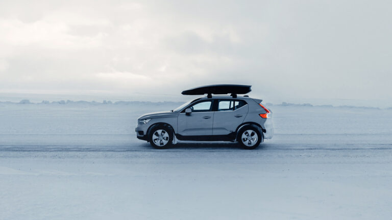 Denna bild visar en Volvo XC40 som kör på en snöig väg. Bilen har en takbox på taket. Takboxen är från Thule och är av modellen Force XT Alpine 420L One. Bilen är utrustad med vinterdäck för att ge bra grepp på den snöiga vägen.